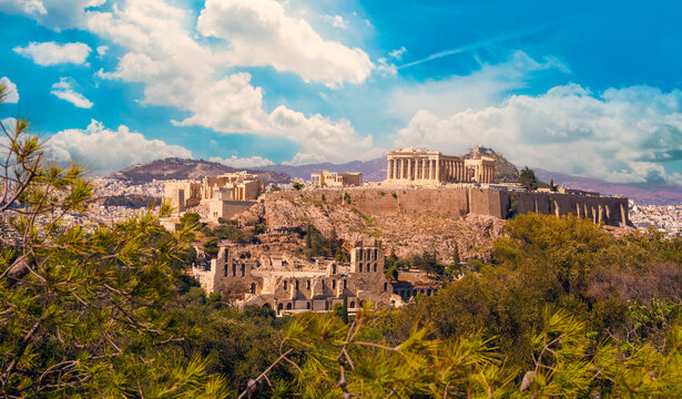 Aerial view of the Acropolis of Athens, Greece, showcasing the Parthenon and the Theatre of Herodes Atticus, in warm Greek summer sunlight, beneath a vibrant blue sky.