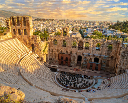 A stunning aerial view of the Odeon of Herodes Atticus in the slopes of the Acropolis, Athens, Greece, with the cityscape in the distance illuminated in the golden glow of the Greek summertime sun