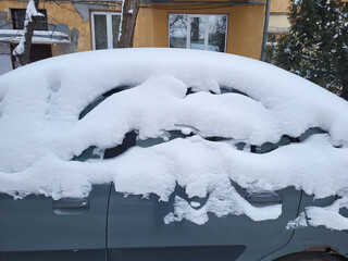 In the parking lot after a heavy snowfall, a blue car covered in snow