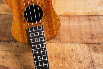 Fototapeta premium A classic brown acoustic ukulele with white wooden strings rests on a rustic wooden table like a folk musical instrument ready to play a jazz and rock music concert