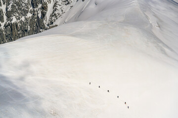 A group of 6 tourist climbers are ascending a snow-covered ridge in the Mont Blanc mountain range in Chamonix France