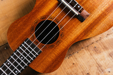 A classic brown acoustic ukulele with white wooden strings rests on a rustic wooden table like a...