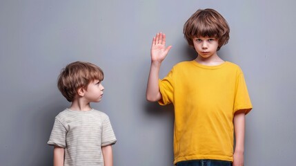 Two children standing against a neutral background, older child raising hand while younger looks up.