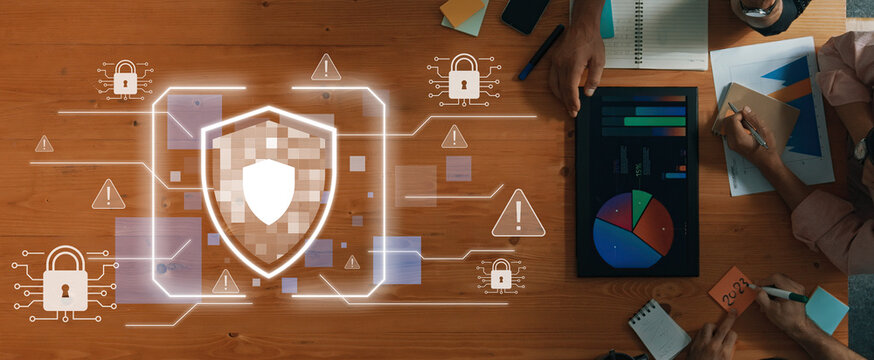 A visually engaging depiction of cybersecurity concepts featuring a digital shield, data analytics, and teamwork on a modern workspace table showcasing security measures. Trope - Powered by Adobe