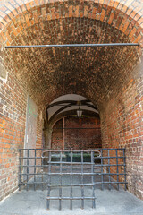 A brick archway with a metal gate in front of it. The gate is open and the archway is empty