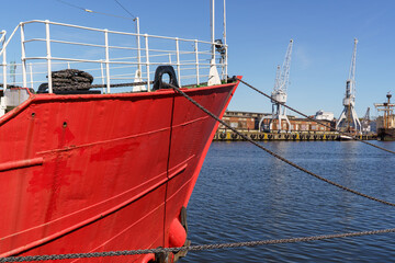 The bow of a red ship parked in the city of Lubeck, Germany. Port cranes are visible in the background