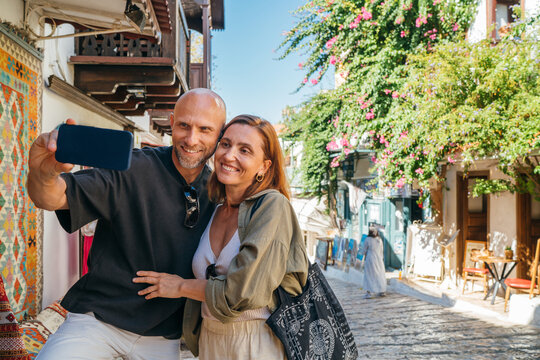 Middle aged couple smiling while making selfie with smartphone narrow street in Kas town historical center. Romantic travel love relationship, honeymoon vacation and happy retirement lifestyle concept