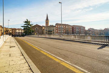 Asphalt road on the bridge over the Adige River in Verona, Italy Part of the city panorama is visible in the background