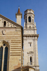 The cathedral complex in Verona, Italy. The building is made of white stone. The tower is visible on the right The sky is blue and bright.