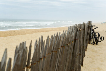 A wooden fence is on the beach in France, with a row of bicycles leaning against it