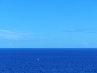 A single white speed boat is cruising across the vast, deep blue ocean leaving a white wake, under a cloudy, blue-grey sky with light pink highlights, ideal for themes of travel, adventure, and freedo © Ena