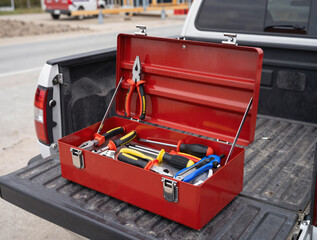 Naklejka premium Open red metal toolbox on a truck bed filled with hand tools at a construction site