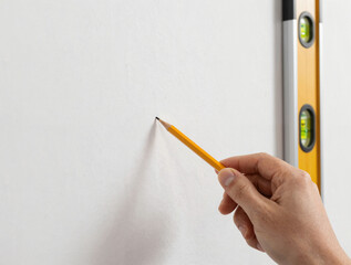 Close-up of a hand marking the center of a stud on a white wall with a pencil and a vertical spirit level nearby