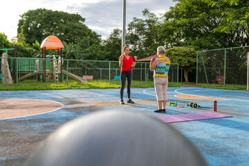 Senior woman doing dumbbell exercises with personal trainer outdoors