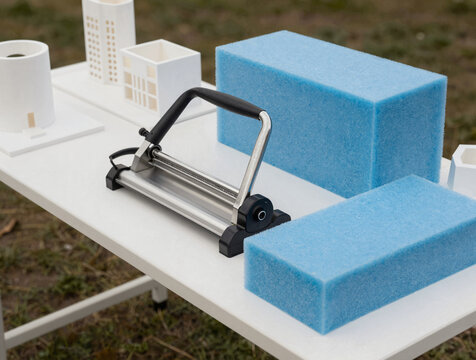Outdoor craft workstation with blue foam insulation blocks, a hot-wire cutter, and white architectural models on a white table