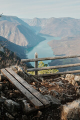 Wooden bench and fence on rocky viewpoint overlooking Drina River canyon and Perucac Lake in Tara National Park, Serbia. Mountain landscape with steep slopes and water.