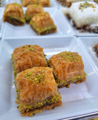 Traditional Turkish baklava dessert with crispy layers of phyllo pastry and ground green pistachios served on a white plate under bright light in a local authentic sweet shop display