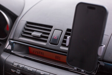 Fototapeta premium Smartphone mounted in car dashboard holder, displaying radio frequency, with air vents and control panel visible, illustrating modern vehicle technology and convenience