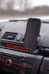 Fototapeta premium Smartphone mounted in a car dashboard holder, showcasing a sleek design and modern technology, with a blurred road view in the background, emphasizing convenience and safety