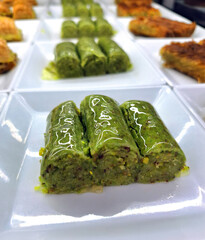 Traditional Turkish pistachio wrap dessert with bright green ground nuts and thin dough rolls served on a white plate in a pastry shop with a sweet syrup and very delicious appearance