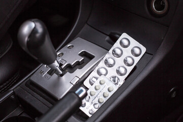 Close-up view of automatic car gear shift with pill blister pack placed beside it, highlighting the intersection of automotive and health themes in a vehicle interior