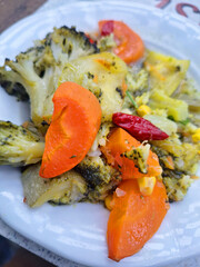 Freshly steamed healthy vegetables including broccoli and carrots served on a white plate as a side dish in a restaurant with bright natural lighting and focus on the green colors