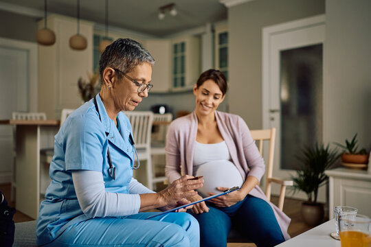 Obstetrician nurse analyzing pregnant woman's medical reports during a house call.