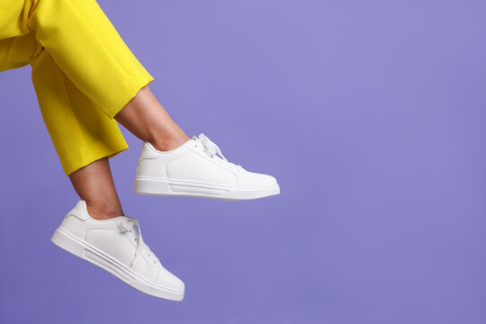 Woman wearing stylish white sneakers on violet background, closeup. Space for text