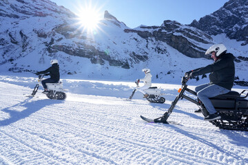 Group of people riding electric snow bikes on a groomed winter trail in the mountains, enjoying outdoor adventure on a bright sunny day
