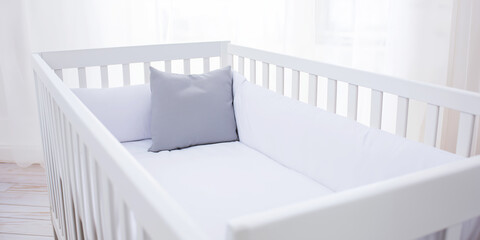 Empty white baby crib with soft bedding, ready for a newborn, creating a calm and peaceful nursery scene