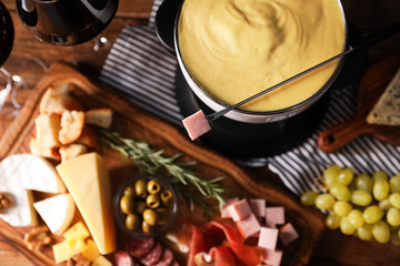Fondue with tasty melted cheese and snacks on wooden table, selective focus