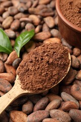Cocoa powder in wooden spoon and green leaves on beans, closeup