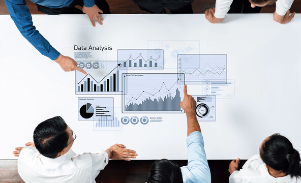 Business professionals engage in data analysis, actively discussing insights while reviewing charts and graphs on a modern workspace table for informed decision-making. Trope - Powered by Adobe