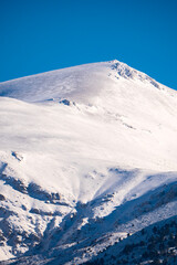 The majestic summit of a snow covered mountain stands tall against a vibrant blue sky during a clear winter day featuring pristine white slopes and dramatic high altitude light