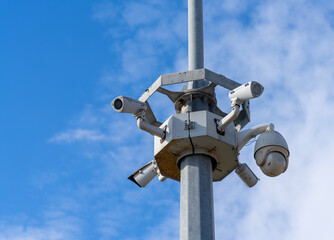 Group of modern surveillance cameras mounted on a metal pole against a blue sky