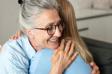 Elderly mother shares a warm hug with her adult daughter at home on a weekend