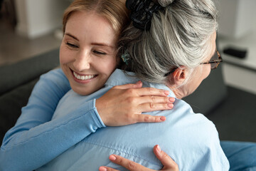 Elderly mother and adult daughter share a warm hug in their living room
