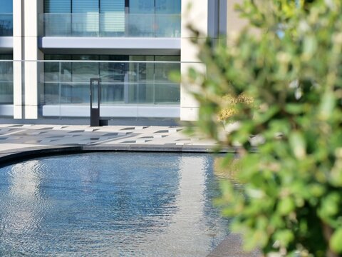 Modern outdoor water feature or pool with a patterned stone surround and view of contemporary apartment or office building facade with glass railings and balconies, for themes of urban lifestyle, desi - Powered by Adobe