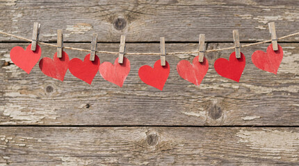 Red paper hearts hanging on clothesline against wood background