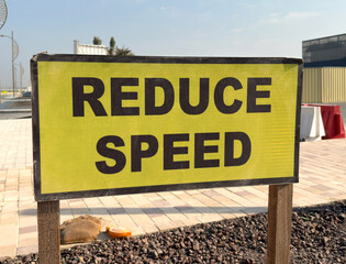 Fototapeta premium Urban road sign with bold Reduce Speed warning for traffic safety in modern city infrastructure. 