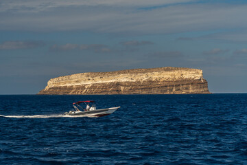 Obraz premium Speedboat passing isolated rocky island in deep blue ocean
