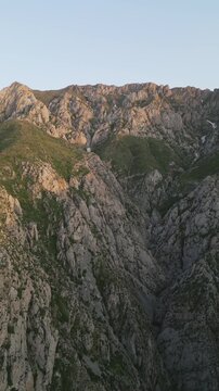 Golden evening light glides across a rocky canyon and green alpine meadows in the Ugam-Chatkal mountains of Uzbekistan, the drone follows ridges and gullies, revealing snow patch and a winding trail