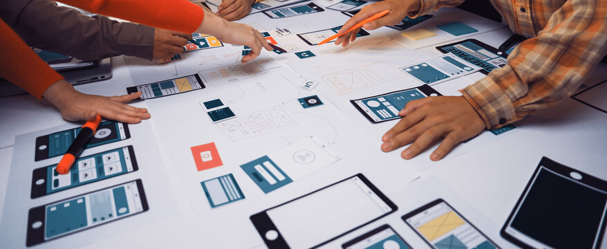 A group of professionals engages in a collaborative effort to design wireframes and user interfaces for a mobile application, utilizing sketches and creative strategies. SACTR