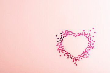 Heart shape made of pink confetti on soft pink background with copy space. Top view, flat lay