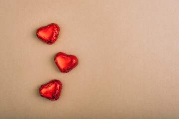 Three red foil wrapped chocolate hearts on brown paper background with copy space