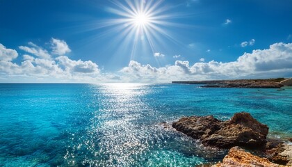 bright sun reflecting on crystal clear blue ocean with white clouds and serene rocky coast