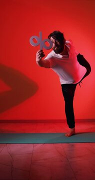 A bearded Caucasian man stands in the Natarajasana (King of Dance) yoga pose while holding a percentage symbol, filmed in a vertical 4K video with a red color filter. The footage combines balance, str