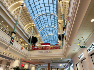 Naklejka premium Indoor Trafford Centre shopping mall atrium with glass skylight, festive decorations, and Be's Cookies cafe in Manchester