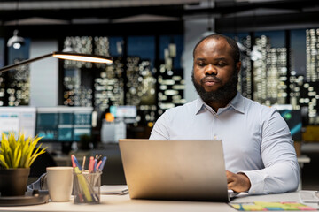 Obraz premium Black man proofreading and fact checking financial numbers, reviewing archived files after hours in the strategy room. Evaluating data on reports, researching and organizing agenda.