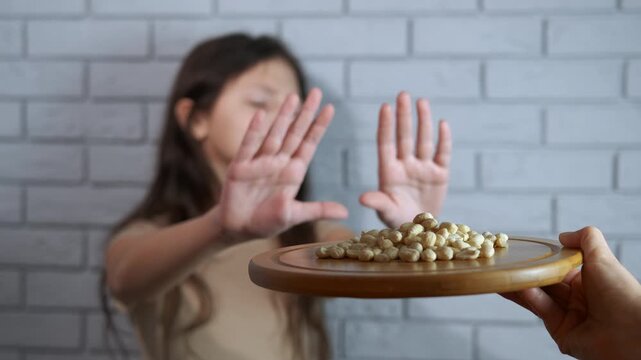 Young girl refusing peanuts showing allergic reaction concept. Serious young girl gesturing with her hands to refuse a plate of peanuts, symbolizing a food allergy